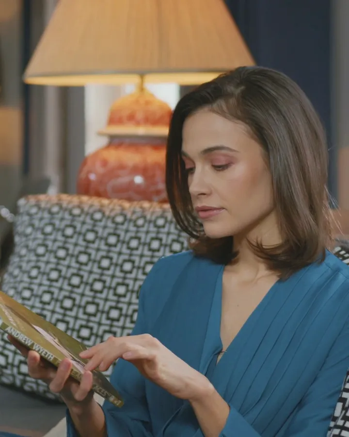 A woman reading a book on a sofa by lamplight in the evening
